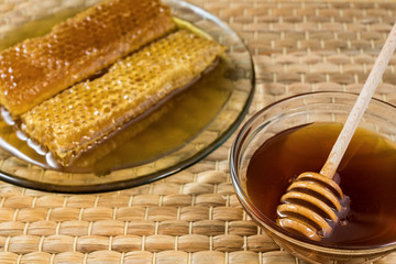 Honeycomb and honey in glass bowl with wooden honey dipper on natural matting