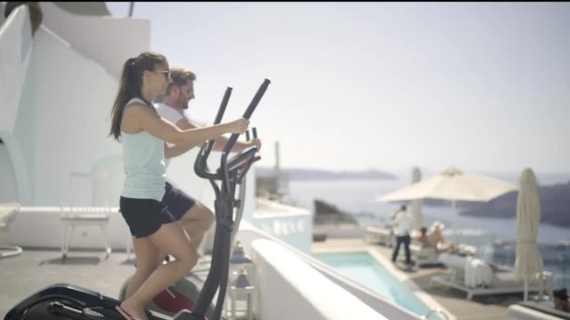 honeymoon couple doing sports on terrace of luxury hotel high up on santorini island
