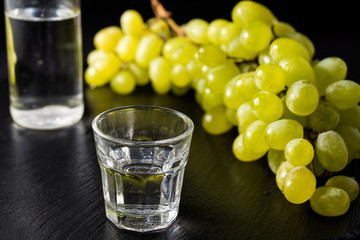 Glasses and  bottle of traditional drink Ouzo or Raki on black dish with a branch of grapes