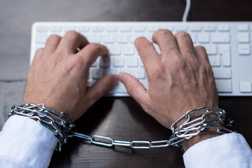 Businessman hands tied with chains on laptop keyboard