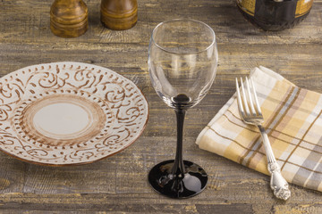 A glass of wine on a wooden background table, with a plate with a fork. A bottle of wine and accessories