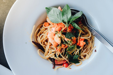 spaghetti pasta with shrimps and sweet basil on white plate over wooden table