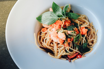 spaghetti pasta with shrimps and sweet basil on white plate over wooden table