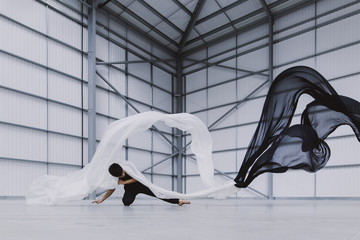 A male dancer performing floorwork with black and white sheets of silk waving around him