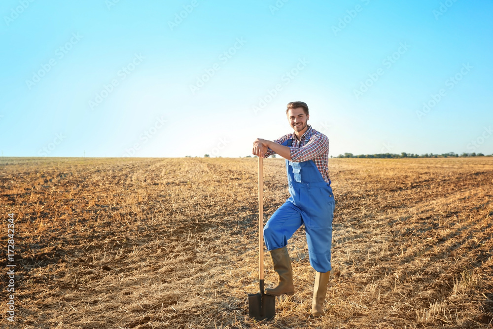 Wall mural Young male farmer with shovel in field