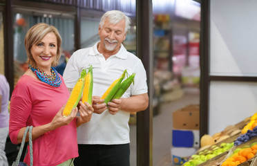 Happy senior couple choosing corn at market