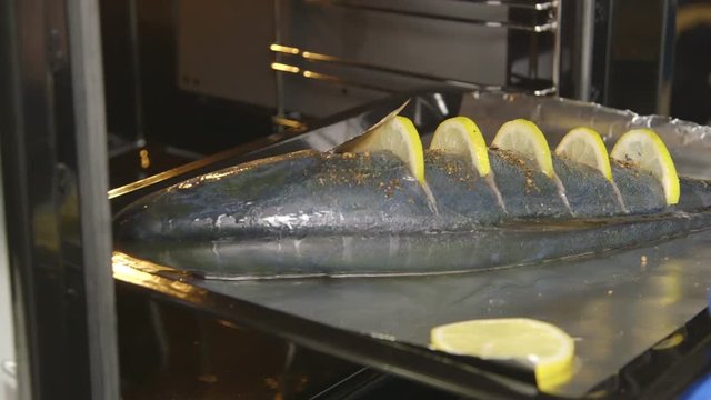 Cooking whole roasted fish seriola with lemon baked in the oven. Chef puts a baking sheet with raw amberjack into the hot oven. Food preparation with electric cooker.
