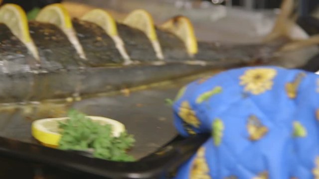Cooking whole roasted fish seriola with lemon baked in the oven. Chef takes out baking sheet with cooked amberjack from the oven. Food preparation with electric cooker.