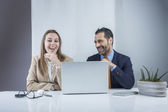 Colleghi  vestiti eleganti ridono felicemente, seduti alla scrivania del loro ufficio davanti al computer.