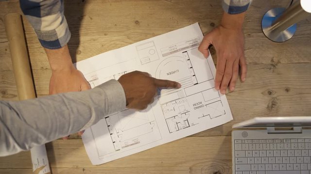 Unrecognizable team of architects in a meeting looking at floor plan. Overhead view looking down at workspace.