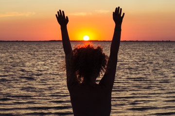 The girl raising her hands to the red sunset at sea, enjoying nature and freedom