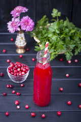 Cranberry juice in a glass bottle and raw cranberry on black wooden background, close up