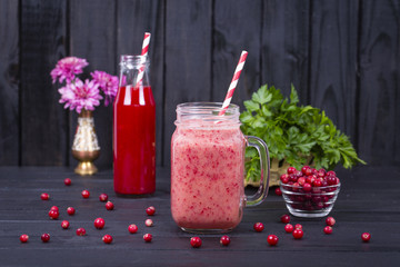 Cranberry juice smoothie shake in glass mug and raw cranberry on black wooden background, close up