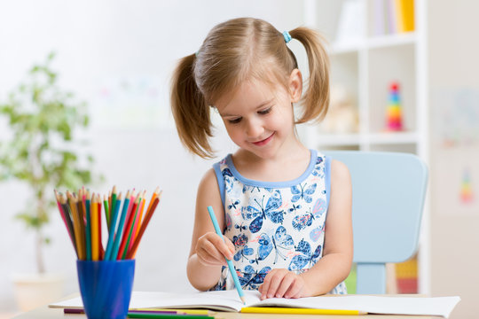 Child girl drawing with colorful pencils in nursery