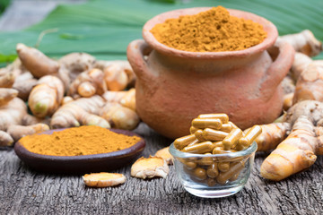 Turmeric powder in clay pot , turmeric capsules and fresh turmeric root on wooden background