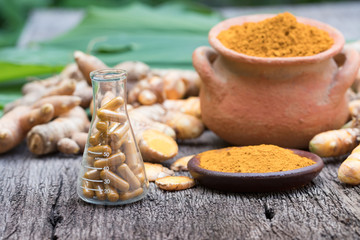 Turmeric powder in clay pot , turmeric capsules and fresh turmeric root on wooden background