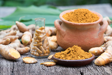 Turmeric powder in clay pot , turmeric capsules and fresh turmeric root on wooden background