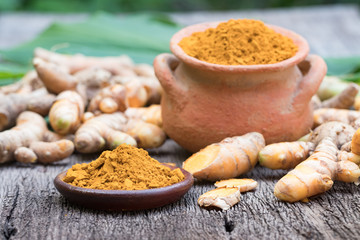 Turmeric powder in clay pot , turmeric capsules and fresh turmeric root on wooden background