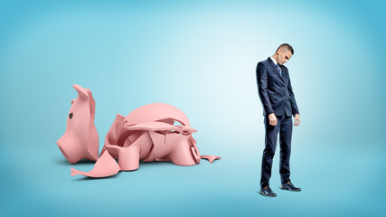 A sad businessman stands turned away from a giant broken piggy bank.