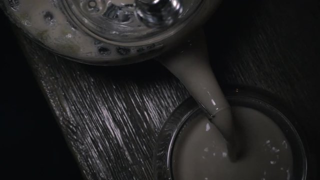 Close-up shot of pouring Indian masala tea from glass tea-pot into a tea bowl. Top view
