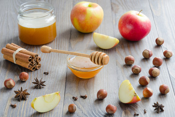 Bowl of honey with honey stick, cinnamon, hazelnuts, apples and spices