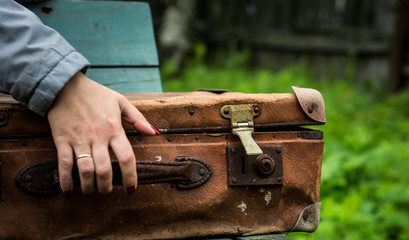 The girl's hand rests on an old suitcase.
