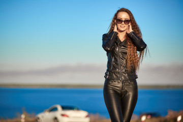 beautiful sexy girl with long hair in a leather jacket and leather pants in sunglasses gets out of...