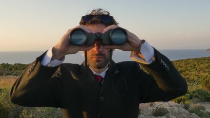 Man in elegant suit with briefcase looking through binoculars on top of a cliff on an island - Powered by Adobe