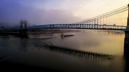 Fototapeta premium A barge on the Ohio River passing under the Roebling Bridge during the early morning, Cincinnati, Ohio, USA