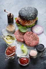 Raw burger cutlets, black hamburger and cooking components. Selective focus, vertical shot