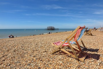 Fototapeta na wymiar Striped deck chairs on pebble beach in Brighton, England, UK with Brighton West Pier in distance