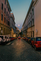 Fototapeta na wymiar Rome, Lazio, Italy. May 26, 2017 : Typical narrow cobbled shopping street of Rome, Italy. With people walking at dusk