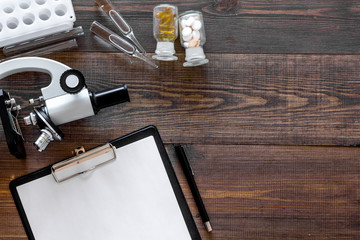 Doctor's workplace. Microscope, pills, tablet, ampoulie on wooden background top view copyspace