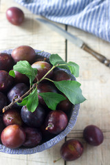 Plums in a clay bowl on a wooden table. Rustic style, selective focus.