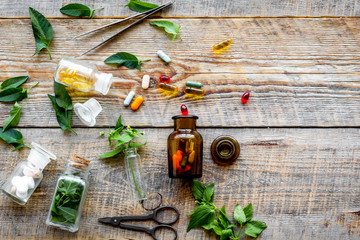 Harvest medicinal herb. Leaves, bottles and sciccors on wooden background top view copyspace