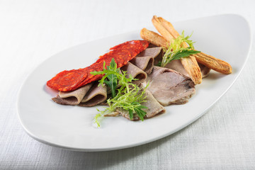 Cold smoked meat plate with pork chops, prosciutto, salami and bread sticks on white wooden background. From top view
