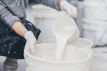 Hands with plastic gloves pouring glazing paint into bucket