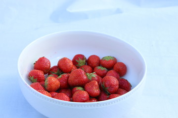 Fresh strawberries in a white porcelain bowl on white table in rustic style, selective focus