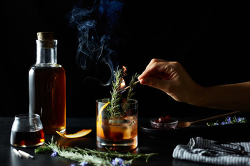 Woman's hand holding burning match in glass of maple cocktail