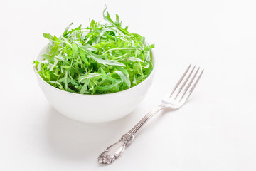 Green salad in a white porcelain bowl on a white table, horizontal