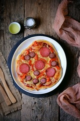 Homemade pizza with smoked sausage, salami and red pepper on a wooden background. Rustic style.