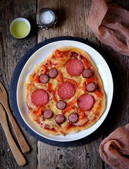 Homemade pizza with smoked sausage, salami and red pepper on a wooden background. Rustic style.