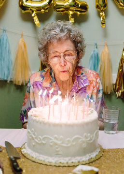elderly woman blowing out birthday candles on cake