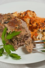 Baked meatloaf with roasted red peppers and cauliflower puree on a round, white dish and a sprig of parsley, and an artisan fork-paleo diet