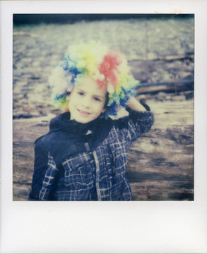 Boy in rainbow clown wig takes a break by leaning against a log