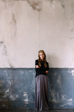 Young woman standing against old wall