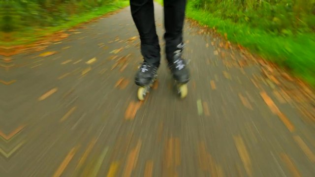Outdoor inline skating on wet slippery asphalt in autumnal forest. Man legs in black running trousers. Quick movement of inline boots on road covered with autumnal ccolorful leaves.. 