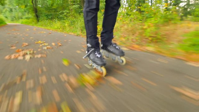 Outdoor inline skating on wet slippery asphalt in autumnal forest. Man legs in black running trousers. Quick movement of inline boots on road covered with autumnal ccolorful leaves.. 