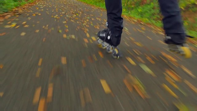 Outdoor inline skating on wet slippery asphalt in autumnal forest. Man legs in black running trousers. Quick movement of inline boots on road covered with autumnal ccolorful leaves.. 
