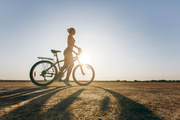 Fototapeta premium A silhouette of a strong woman in a colorful suit that sits on a bicycle in a desert area. Fitness concept. Blue sky background